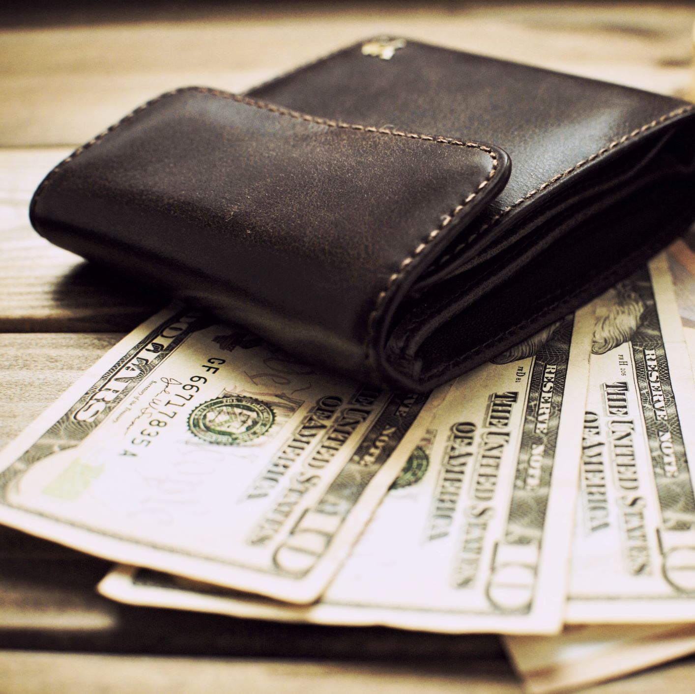 Photo of a wallet sitting on top of multiple ten dollar bills