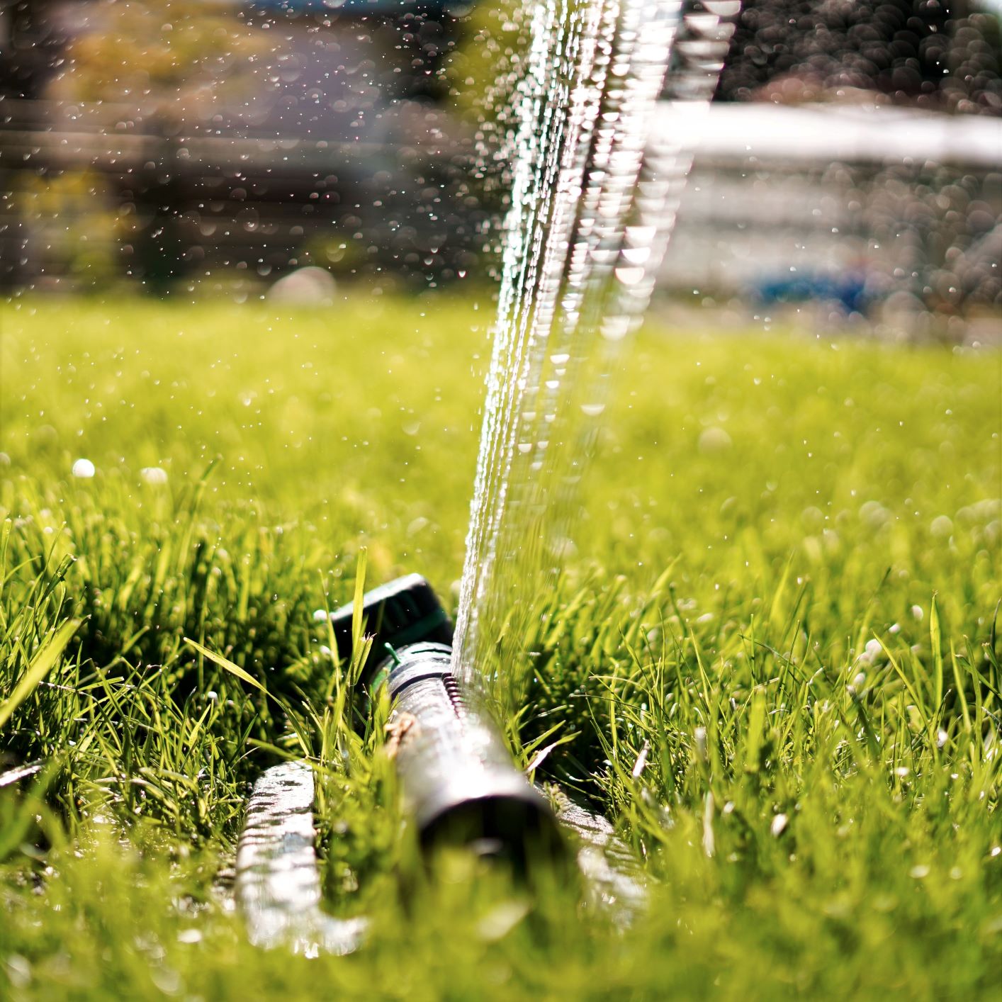 Photo of a sprinkler with water flowing out of it onto green grass.