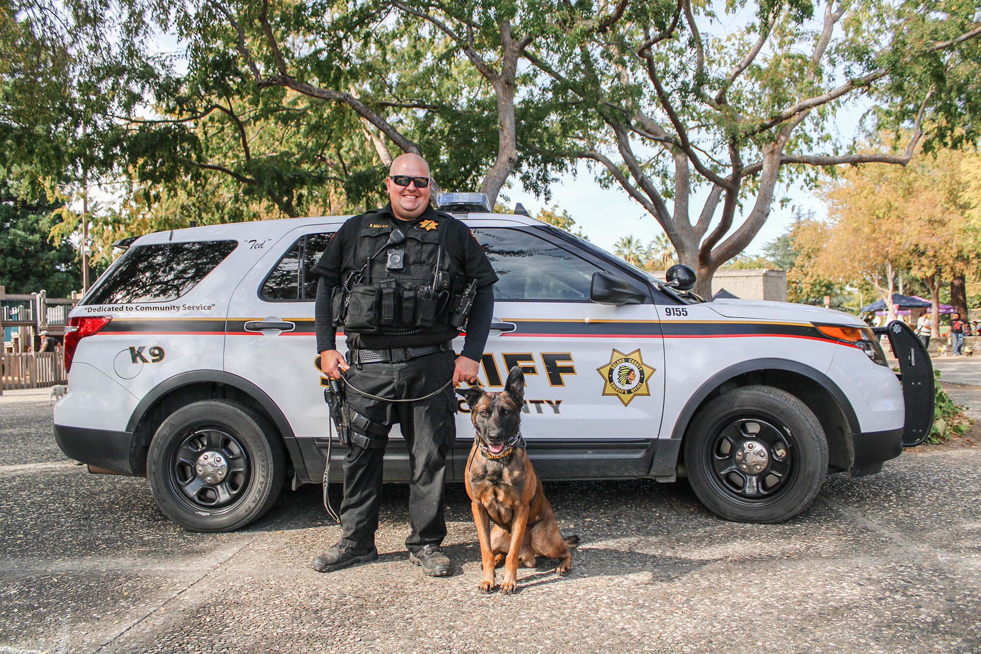 Sheriff and his K9 officer stand in front of a white Sheriff vehicle