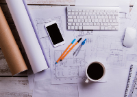 desk with plans, coffee, laptop, pencils