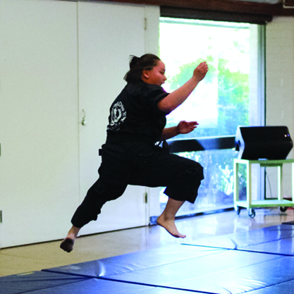 A woman in a black Gi does a Kenpo Karate jump kick