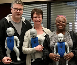 Three people holding CPR dummies.