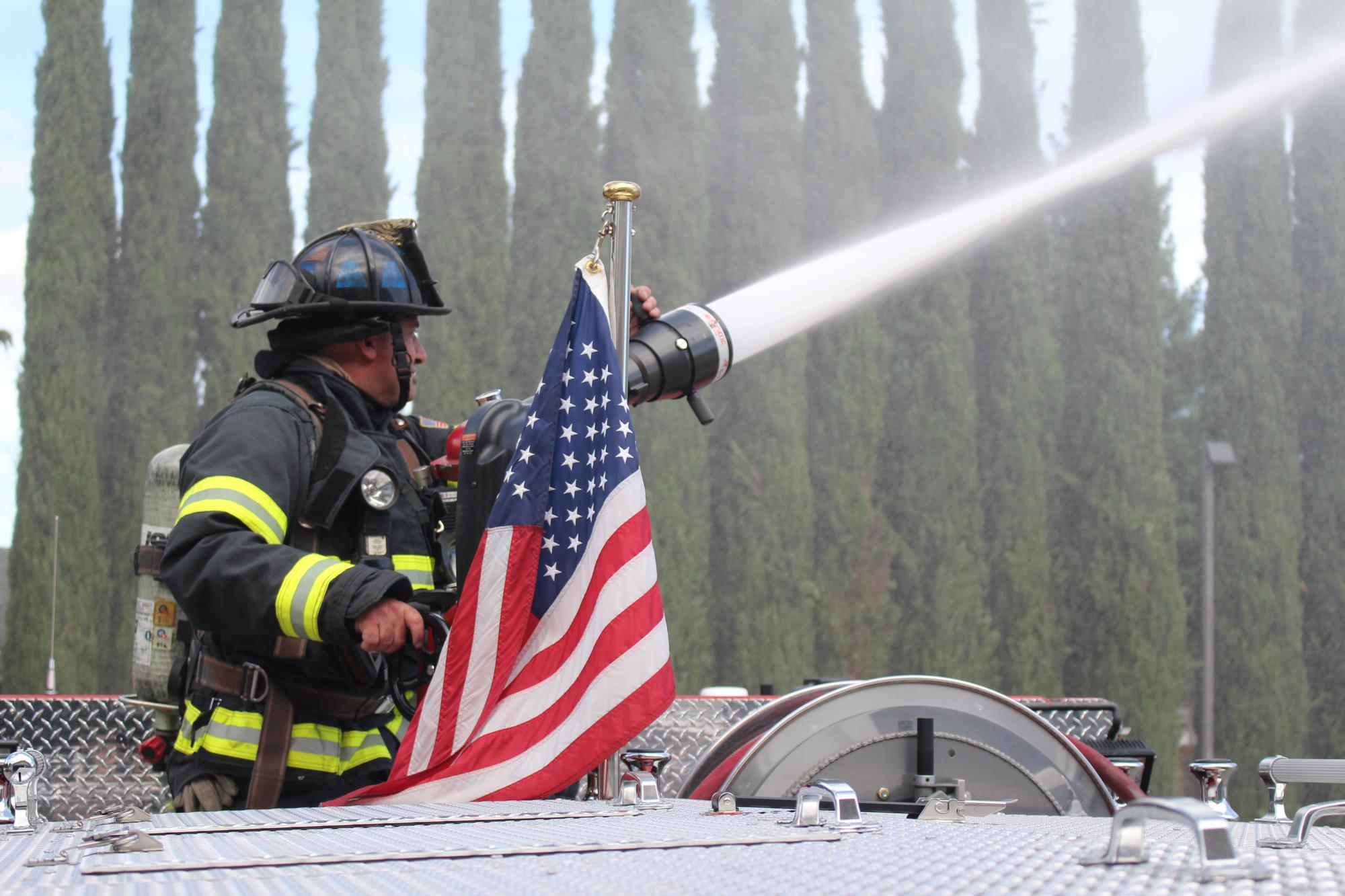 Firefighter spraying water with American flag next to him